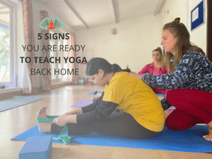 Yoga teacher assisting student in seated forward bend during teacher training at Akshara Yoga School in India